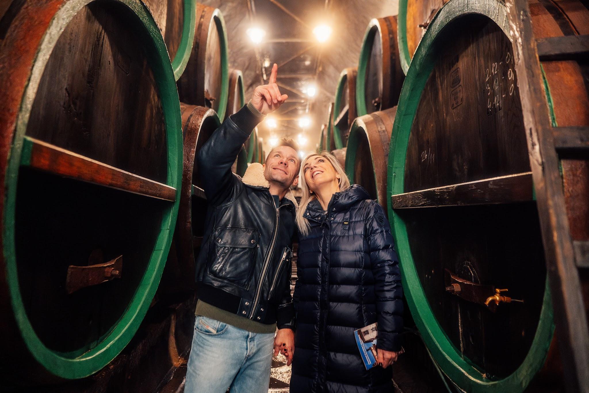 Dos visitantes entre grandes barricas de madera con aros verdes en las bodegas subterráneas de una cervecería