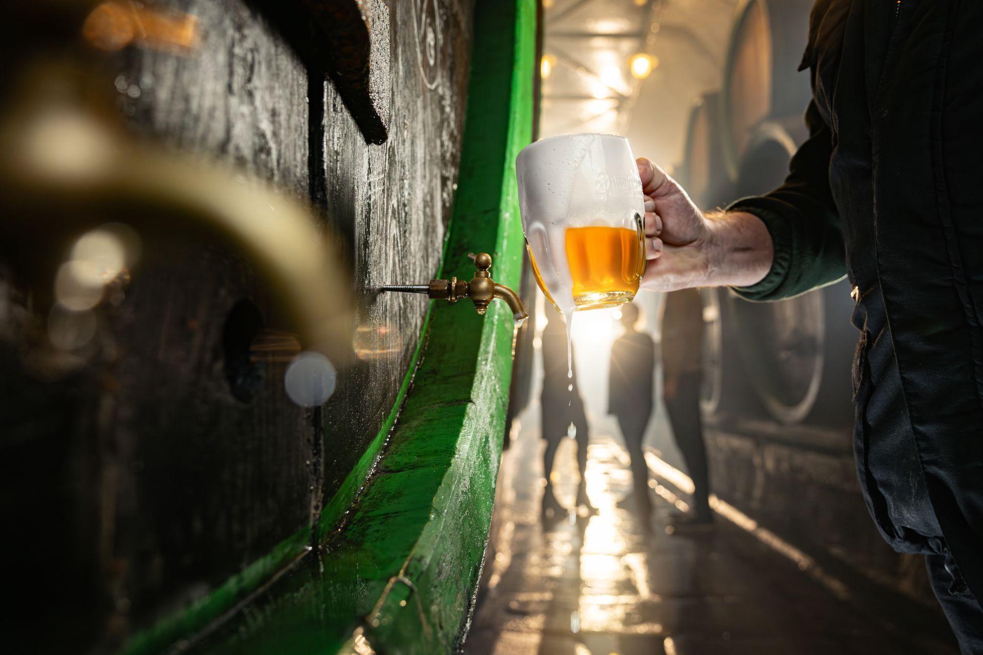 Mano sosteniendo un tarro de cerveza con espesa espuma bajo el grifo de una barrica de madera en una bodega cervecera