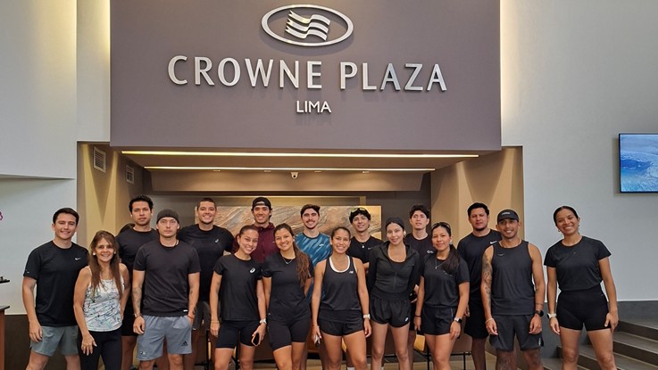 Grupo de más de 20 influencers runners en ropa deportiva negra posan frente a la recepción de Crowne Plaza Lima, bajo el logo del hotel.