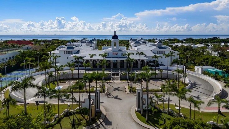 Vista aerea de la entrada principal del Riu Palace Mexico, con su fachada blanca, cupula central y la rotonda de palmeras frente al mar Caribe