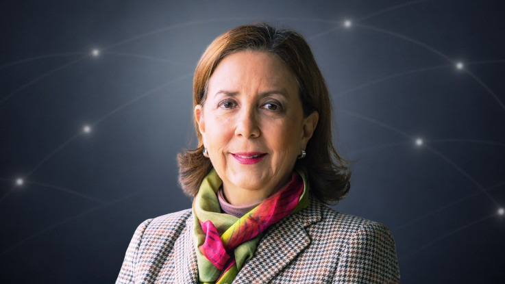 Retrato de una mujer con chaqueta de tweed y pañuelo de colores sobre fondo oscuro con puntos luminosos