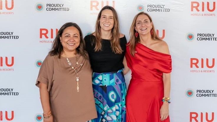 Tres personas posan ante un fondo con los logotipos de RIU Hotels & Resorts y el lema Proudly Committed